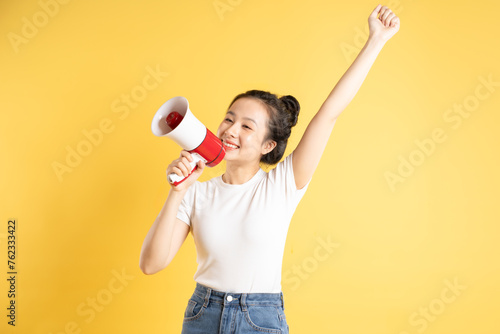 Image of Asian woman holding a portable speaker and posing on a yellow background © L