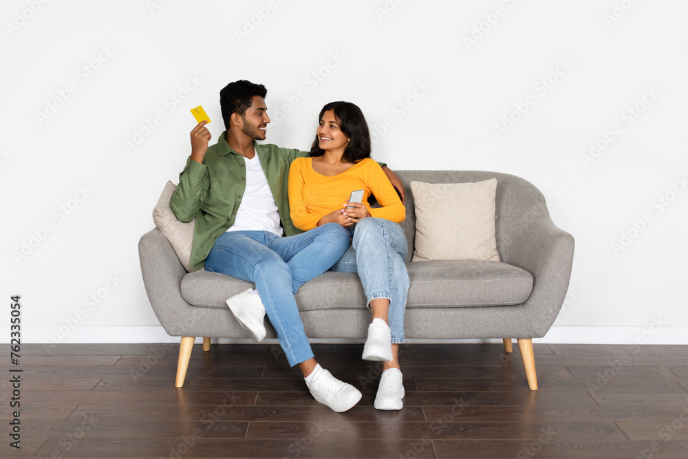Joyful hindu couple with credit card and phone on couch Joyful hindu couple with credit card and phone on couch