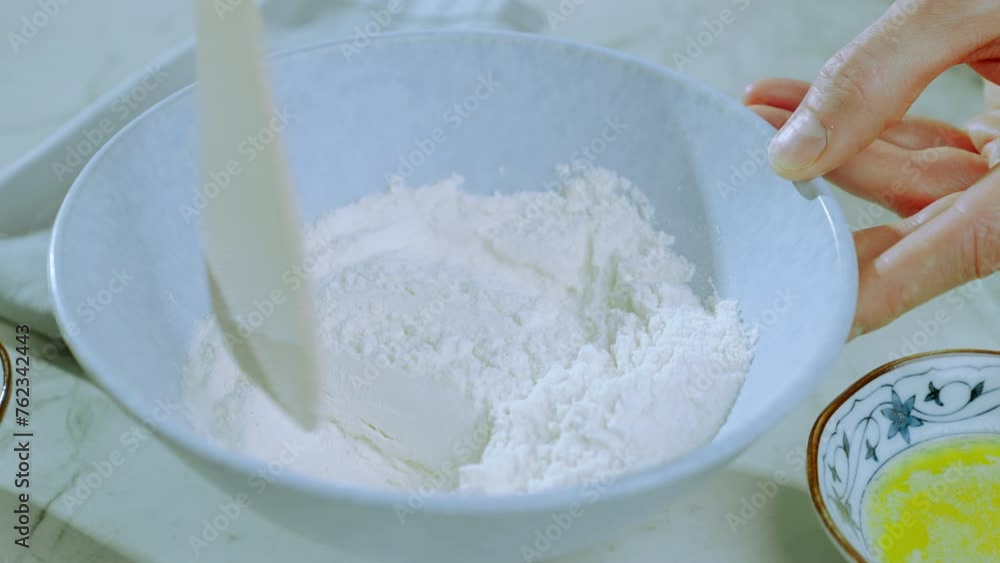 The cook stirs the flour in a light bowl with a wooden spatula. Preparation of pancake batter. Food preparation. Slow motion 100fps. The cook stirs the flour in a light bowl with a wooden spatula. Preparation of pancake batter. Food preparation. Slow motion 100fps.