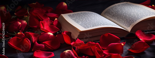 Still life photography of open book with red rose petals scattered on black fabric background