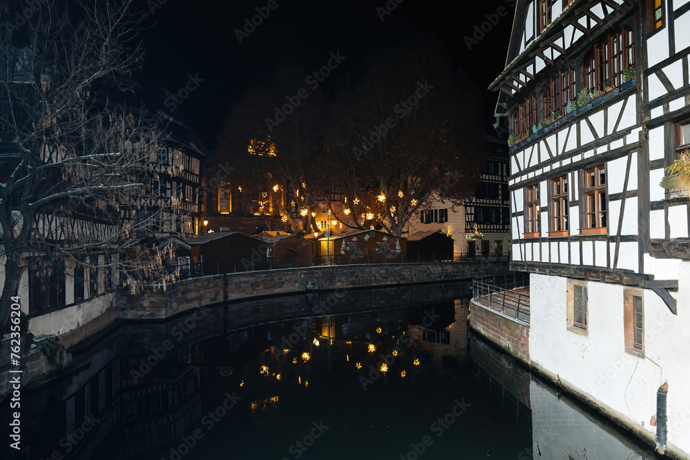 A magical night in Petite France adorned with twinkling stars illuminating the trees, while the Ill River beautifully reflects the charm of Strasbourg, hailed as the best Christmas capital of Europe
