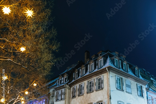 Twinkling star-shaped lights adorning a tree beside European houses at night