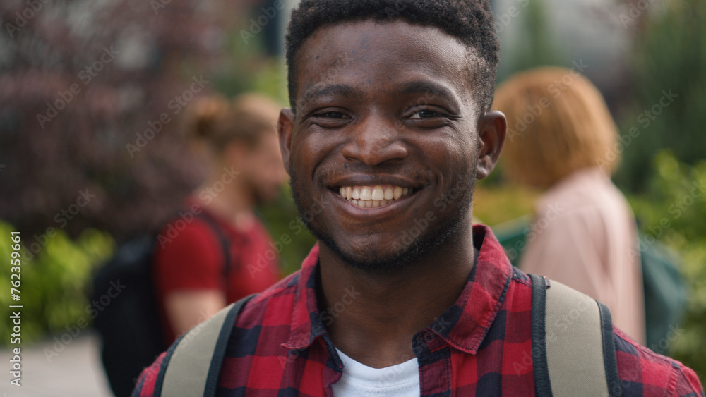 African American young student man guy smiling happy carefree pupil high school schoolboy smile at camera standing on background of talking diverse multiracial students friends education outdoors - obrazy, fototapety, plakaty 