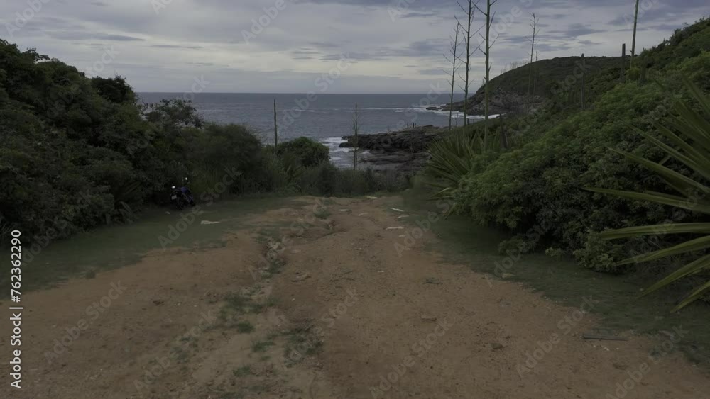 Drone flies low over walking path that leads to beach and rocky cliffs overlooking bay Drone flies low over walking path that leads to beach and rocky cliffs overlooking bay