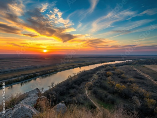 Wide-angle view capturing a breathtaking sunset with dynamic clouds over a winding river flanked by autumn foliage.