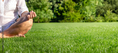 Close up of mature woman meditating on green meadow in the park. Zen concept. 
