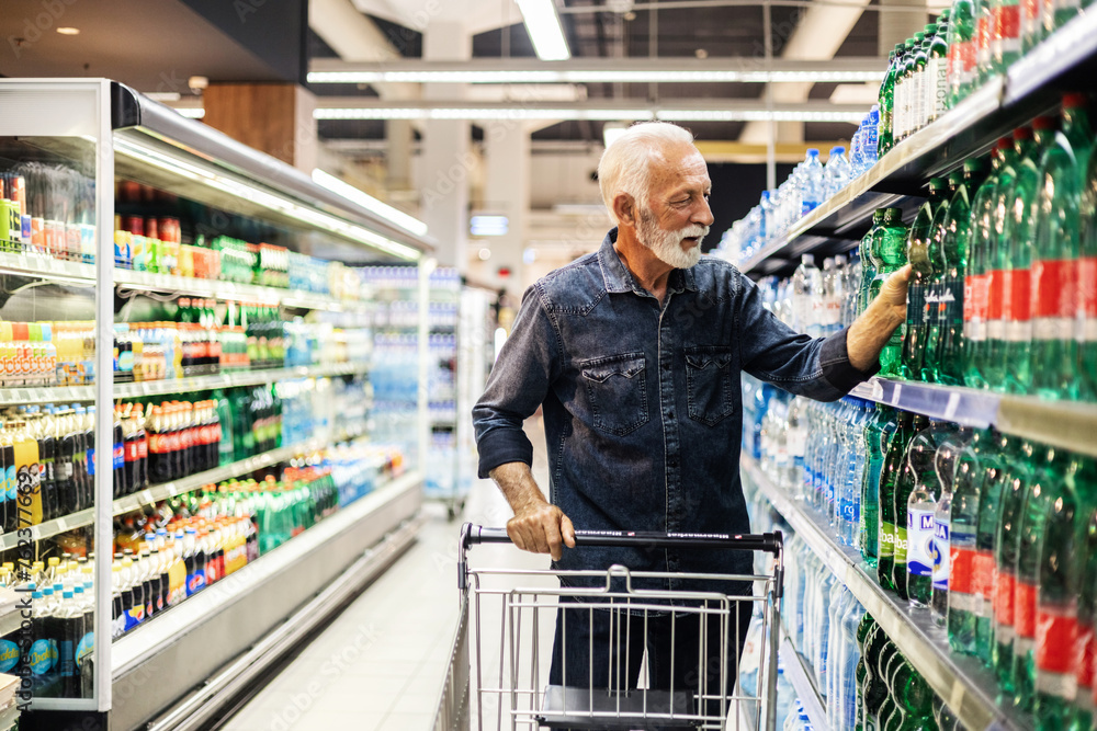 Senior bearded happy male purchasing a bottle of water. Man buying bottled water in grocery store.