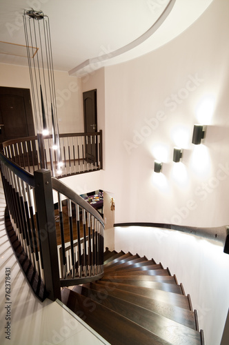 Modern home interior with elegant spiral stairs made of brown woodwork, walls illumination