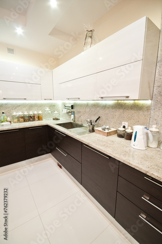 Elegant, modern kitchen inetrior with brown furniture, expensive appliances, illuminated at night. Contemporary home disgn architecture European style.