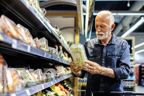 Foto Smiling elderly man picking up vegetables in a grocery store.