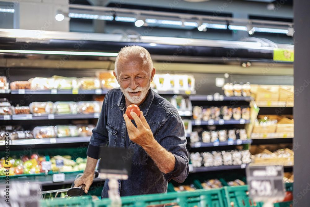 Closeup portrait of a mature man shopping for tomatoes in a grocery store. Senior man carefully selects produce at a grocery store.