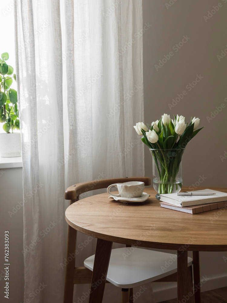 Cozy interior - a bouquet of tulips in a vase, a cup of tea, books on a round wooden table Cozy interior - a bouquet of tulips in a vase, a cup of tea, books on a round wooden table
