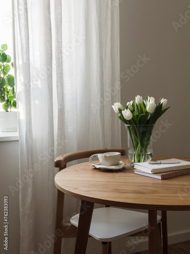 Cozy interior - a bouquet of tulips in a vase, a cup of tea, books on a round wooden table