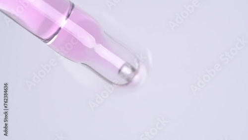 Macro shot of pink oil serum flows from dropper on white background. Skin care cosmetics for body, face or nails. Motion of molecule bubbles in a cosmetic serum photo