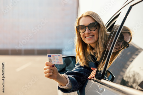 happy young woman showing her new driver license out of car window after successful test at driving school. copy space