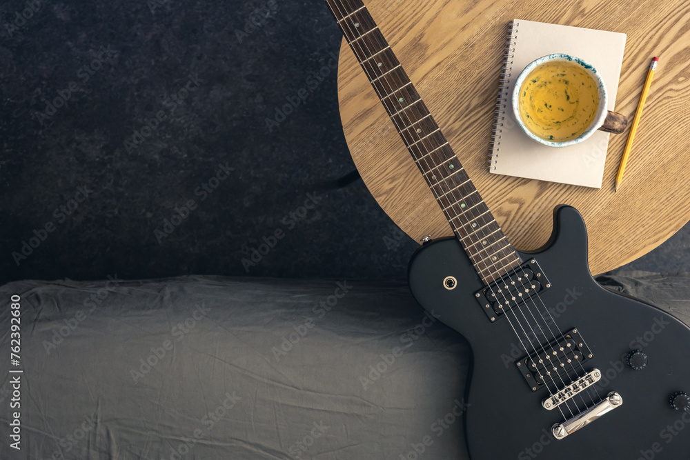 Obraz premium Musical background with electric guitar, notepad and cup of tea on the table.