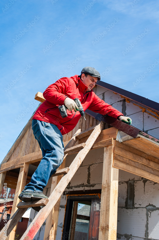A worker builds a roof in a house while standing on a wooden ladder. Blue sky A worker builds a roof in a house while standing on a wooden ladder. Blue sky