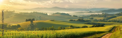 The image shows the sun shining brightly over the rolling hills in a serene landscape. The hills are lush green, and the suns rays create a beautiful contrast with the shadows. © vadosloginov
