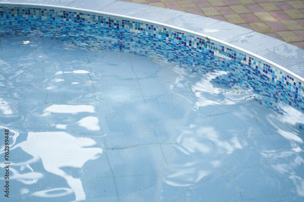 Cropped view of a round outdoor swimming pool with blue mosaic ceramic tiles, with blue water. Background with copy space. Concept of summer, swimming, leisure time, vacation.