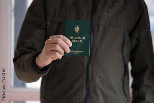 Young ukrainian conscript soldier shows his military token or army ID ticket indoors close up photo