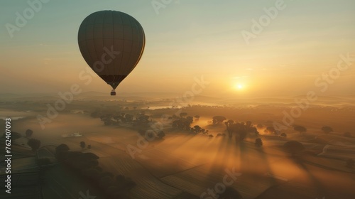 Sunrise Hot Air Balloon Ride Over Misty Fields, first light of day breaks over rolling mist-covered fields, viewed from the serene vantage of a hot air balloon drifting silently in the awakening sky © Viktorikus