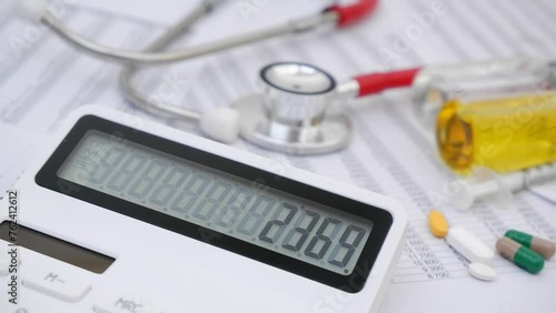 Calculator with changing numbers on display and stethoscope with medical drugs and vaccines on financial data. Cost of medicine and health insurance concept.