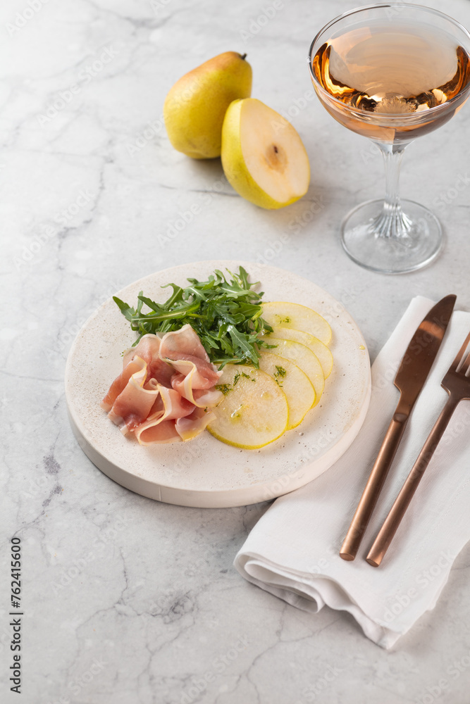 Summer pear salad with prosciutto, arugula on light great marble background. Healthy diet concept. Italian cuisine. Vertical