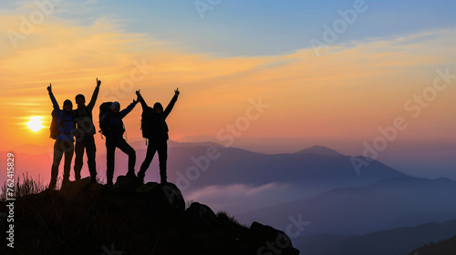 Silhouette of a group of four hikers standing on the top of the mountain with their arms raised up in the air. Happy and successful hiking friends during the twilight sunset, achievement adventure