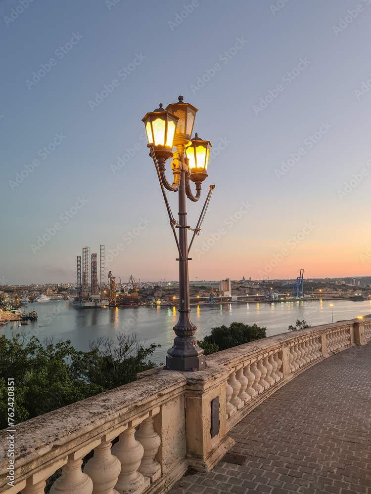 Triq Girolamo Cassar, Valletta, Malta - November 14th 2020: Street light with the Grand Harbour and Paola dockyard in the background.