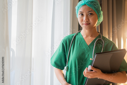 Portrait of female doctor with lab coat in her office holding a clipboard with medical records, she is looking at camera