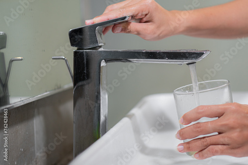 Woman filling glass with tap water from basin