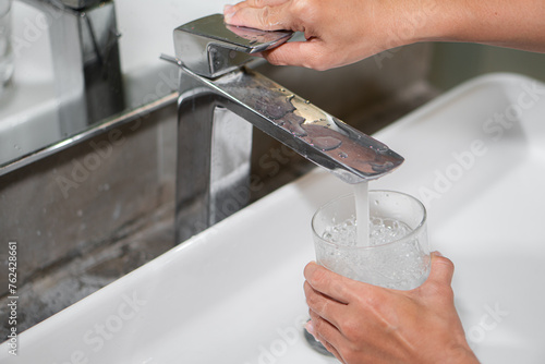 Woman filling glass with tap water from basin