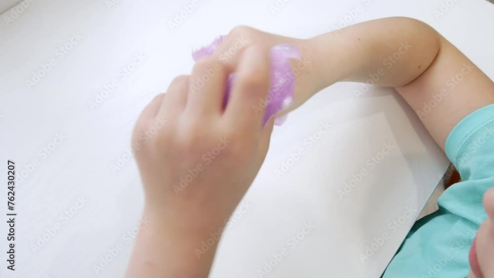 The child's hands are large crumpled and stretched purple slime with large white foam balls is wound into the palm of his hand. The fashionable liquid toy sticks to your fingers. The child's hands are large crumpled and stretched purple slime with large white foam balls is wound into the palm of his hand. The fashionable liquid toy sticks to your fingers.
