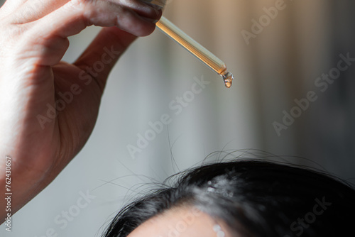 The girl puts on her black hair of hydrolyte from a pipette hair tonic