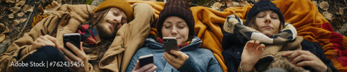 A group of friends in warm clothing lying down together, each engrossed in their own smartphone