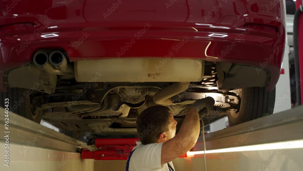 Auto mechanic inspects suspension steering system under car with hydraulic play detector in service. Pro uses remote to check vehicle safety, maintenance work in garage. Diagnostic tools in use. Auto mechanic inspects suspension steering system under car with hydraulic play detector in service. Pro uses remote to check vehicle safety, maintenance work in garage. Diagnostic tools in use.