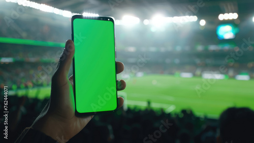 Human hand gripping phone with soccer field in background, intended for clipping path application 