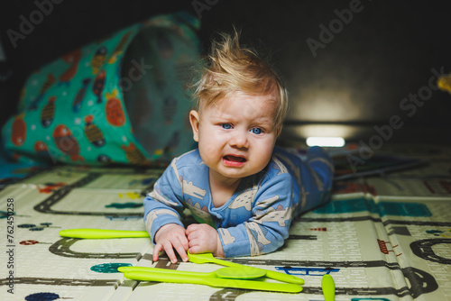 A small child lies on a thermal mat and plays with toys. Carpet for children's games.