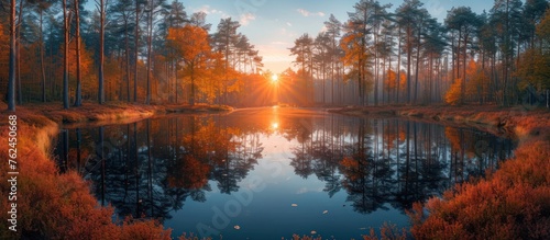 The sun sets on a small forest lake surrounded by trees reflected in the water