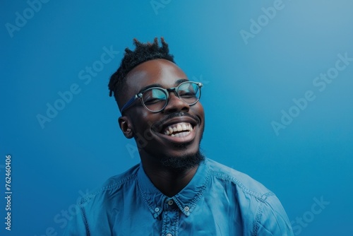 man in glasses wearing a blue shirt smiling against a blue background stock photo