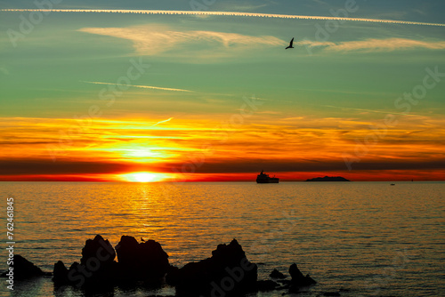 Sunset over the ocean with island and ship in silhouette