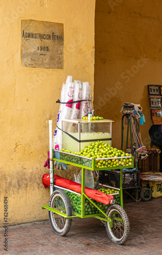 Cartagena, Colombia - July 25, 2023: Fresh lime juice pushcart closeup parked in passage of historic Administracion Roman building. Fresh fruit, iced juice and drinking cups photo