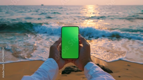 Hand Holding Smartphone with Green Screen on Tropical Beach Backdrop - Ideal for App Mock-ups and Digital Lifestyle © Philipp