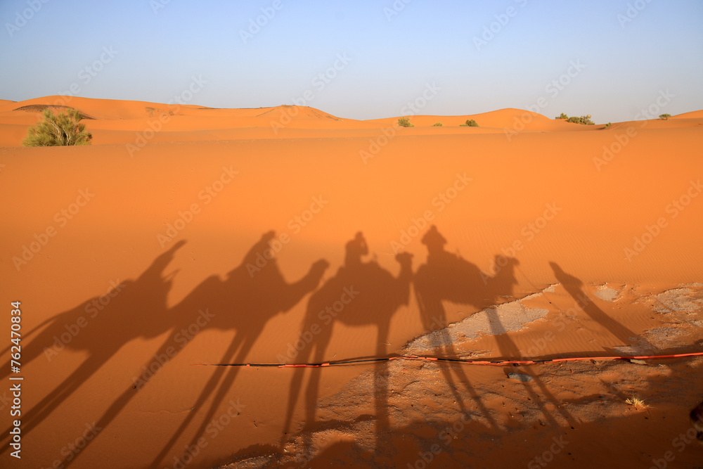 The Sahara Desert in Morocco, Africa, with the silhouette of riders on a camel. - obrazy, fototapety, plakaty 