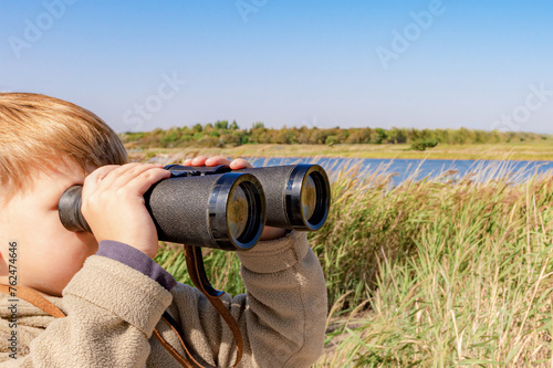 A boy with binoculars in the reeds is watching the wildlife.