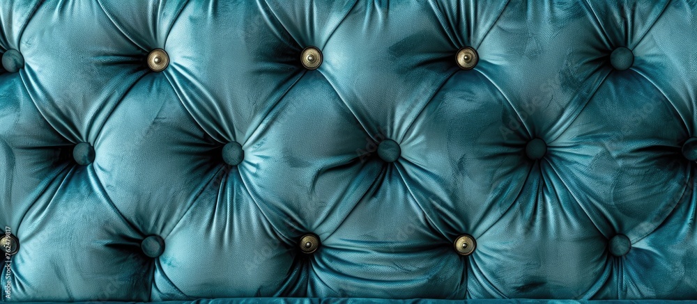 Fototapeta premium A closeup of a tufted couch resembling a cloud on a sunny day, with vibrant blue fabric and elegant gold buttons, reminiscent of the azure sky reflecting in water