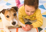 Small girl learning to read. Kid is reading a book to her pet dog.