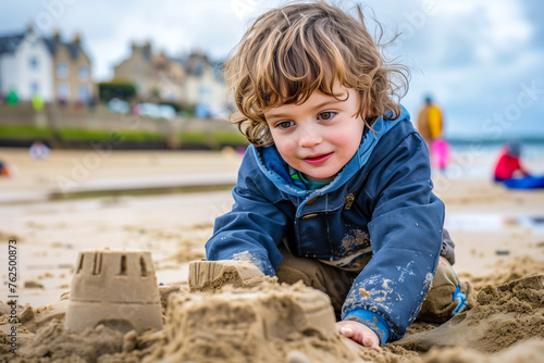 young smiling blond boy building sandcastles on the beach, fun outdoor activity