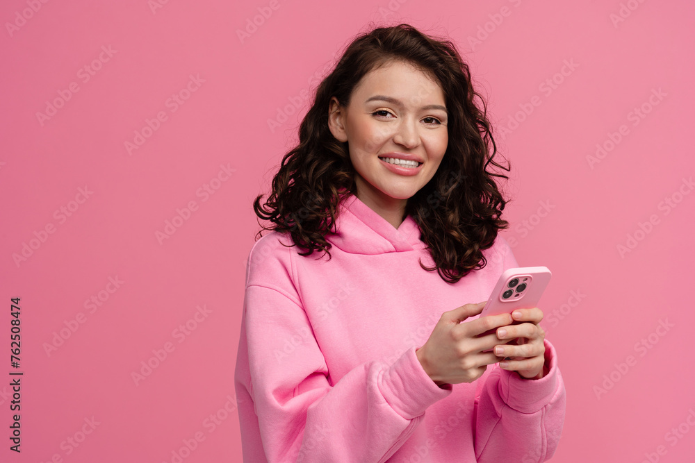 happy smiling woman in pink hoodie posing on pink studio background holding smartphone happy smiling woman in pink hoodie posing on pink studio background holding smartphone