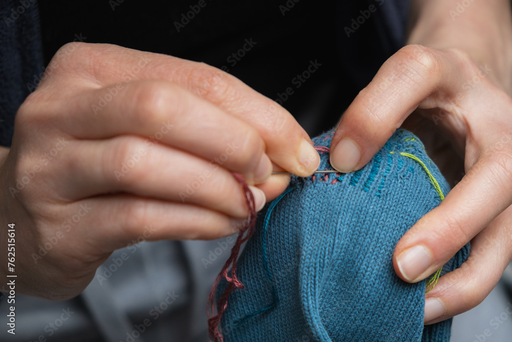 Mending clothes. Visible mending repairing sock. Darning old socks, reducing waste, slow fashion. Repair concept, selective focus. - obrazy, fototapety, plakaty 